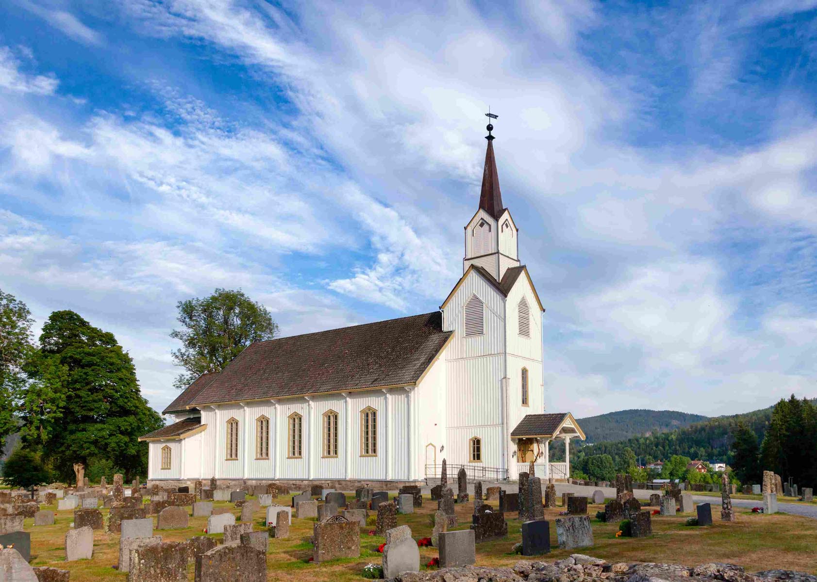 Hvit trekirke i Seljord omgitt av kirkegård og åpent kulturlandskap