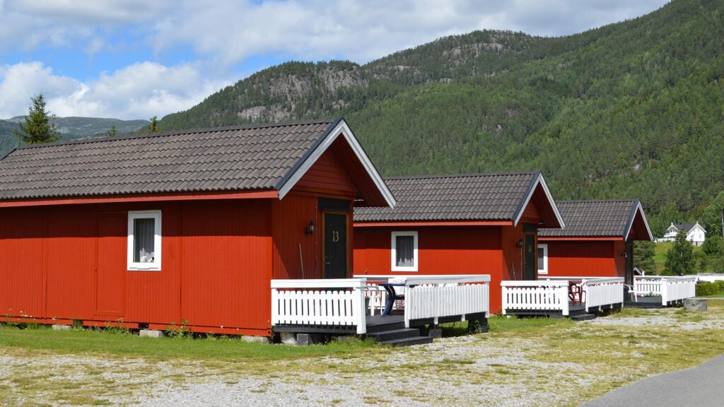  Sanda Campings røde hytter på rekke og rad med hvite verandaer, omgitt av grønne trær og fjell 