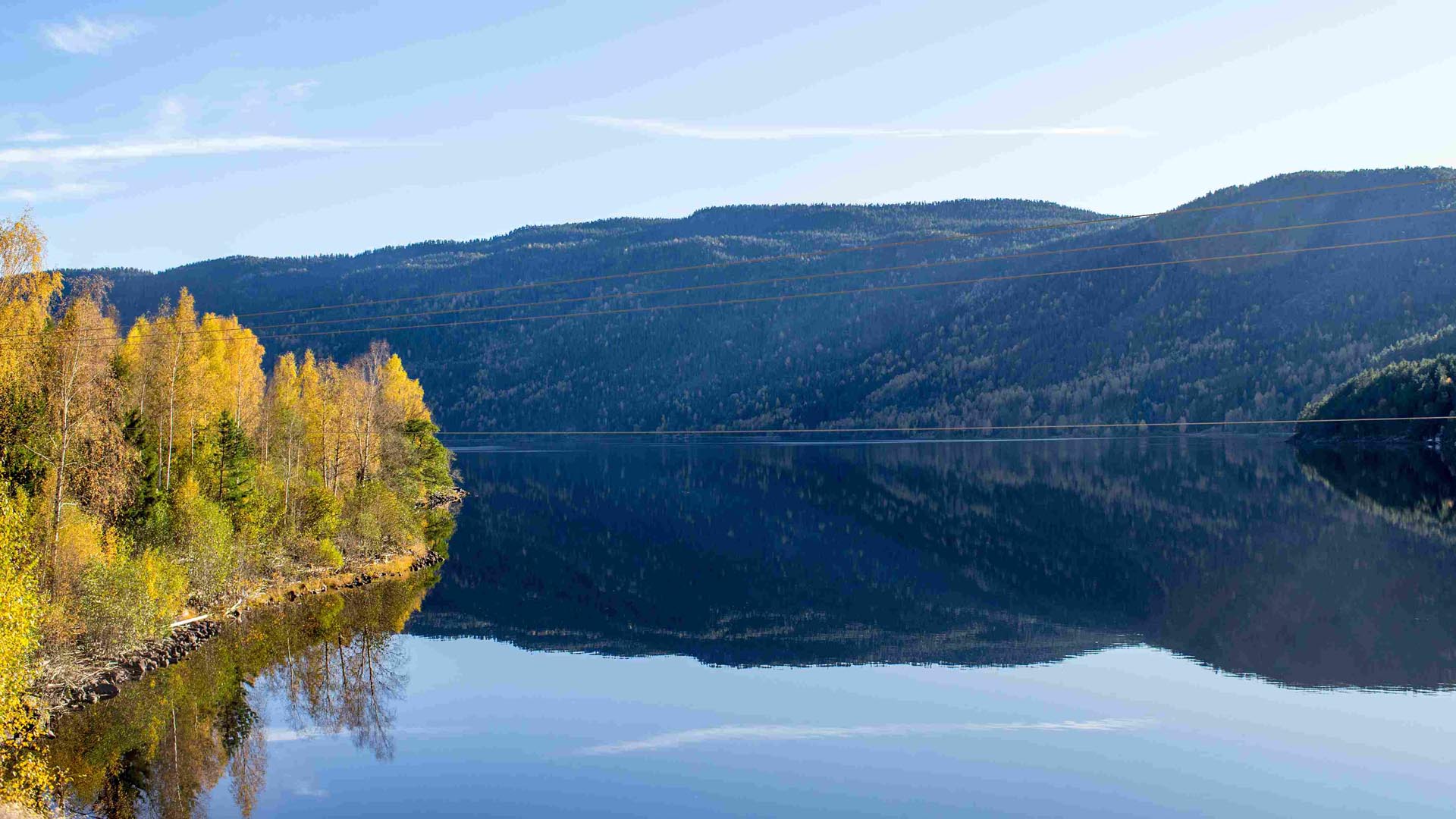 Høstfargede trær speiler seg i stille vann ved Seljordsvatnet, med skogkledde åser i bakgrunnen.